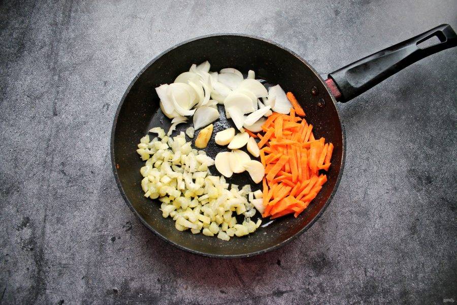 В сковороду налейте растительное масло и выложите нарезанную соломкой морковь. Сельдерей порежьте, чеснок очистите и разрежьте на дольки. Имбирь очистите и выложите в сковороду. Репчатый лук очистите, порежьте полукольцами и добавьте к овощам.