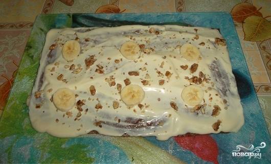 Корж разделите на три части и перемажьте каждую сметанным кремом. Посыпьте орешками, выложите кружочки банана и любые ягоды или фрукты по вашему желанию. Поставьте торт в холодильник минимум на два часа, чтобы он успел пропитаться. 