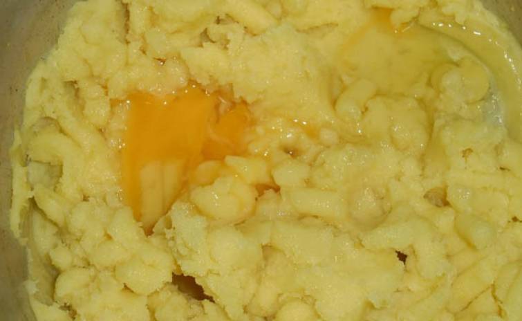 Картофель промойте и очистите, затем отварите в кипящей подсоленной воде до готовности. Слейте воду с картофеля, добавьте сливочное масло и яйцо. Тщательно перемешайте.