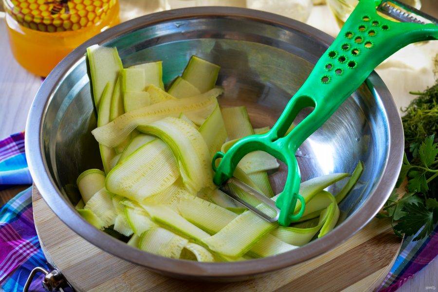 Промойте кабачки, срежьте хвостики. При помощи овощечистки нарежьте кабачки тонкими полосками.