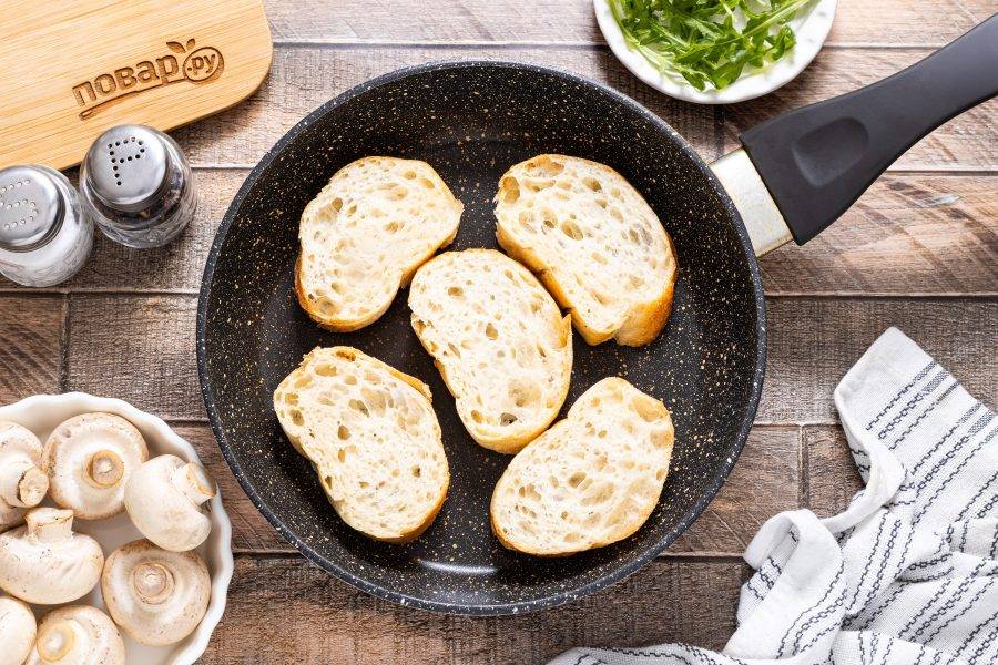 Полейте ломтики багета оливковым маслом и обжарьте с двух сторон до золотистой корочки.