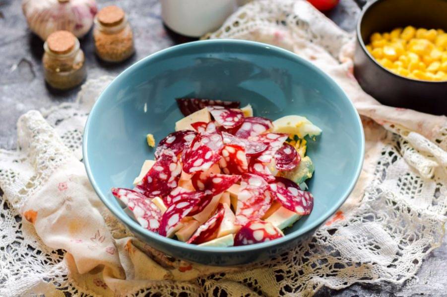 Колбасу нарежьте небольшими кусочками и переложите в салат. Можете заменить колбасу курицей или мясом.