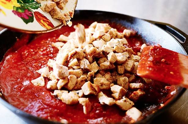 Добавляем томатный соус, слегка прогреваем его, после чего возвращаем в сковороду курицу. Добавляем свежую зелень и тушим 7-8 минут на среднем огне, помешивая.