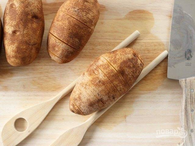 1. Вымойте картофель, затем с помощью двух лопаток, а точнее их ручек зажмите каждый. Острым ножом сделайте глубокие надрезы, но не дорезайте до самого конца.