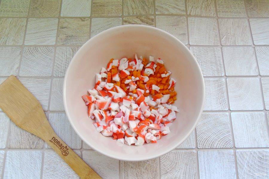 Морковь отварите, охладите и очистите. Нарежьте кубиками морковь и крабовые палочки. Выложите в салатник.