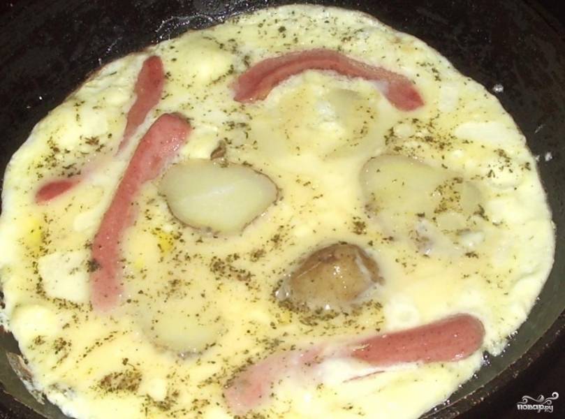 Сначала выложите на сковороду с растительным маслом нарезанный кусками картофель и сосиски. Немного обжарьте и залейте яично-молочной массой.