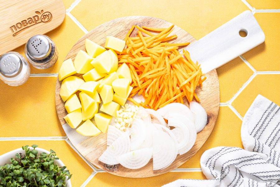 Морковь и картофель очистите от кожуры. Картофель нарежьте кубиками, а морковь натрите на терке. Репчатый лук нарежьте полукольцами, а чеснок очистите и крупно порубите.