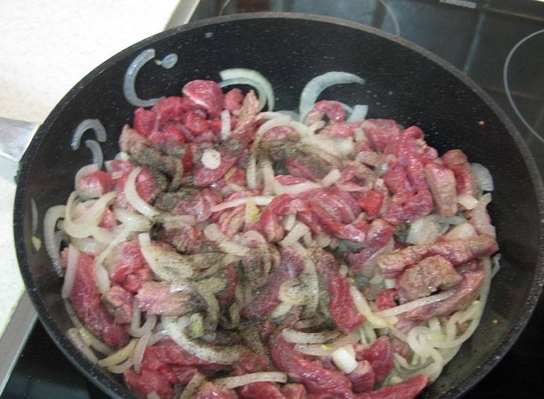 2. Обжариваем мясо, а в середине жарки добавляем лук, нарезанный полукольцами. Жарим говядину до образования легкого золотистого цвета.