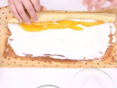 Когда бисквит испекся, достаньте его из духовки и остудите. Распределите крем по всей поверхности и уложите кусочки манго. Скрутите бисквит в рулет и порежьте на порционные кусочки.