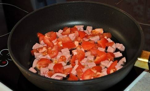 В сковородку наливаем немного масла и хорошенько разогреваем ее. Кладем в сковородку кубиками нарезанные помидоры и колбасу.