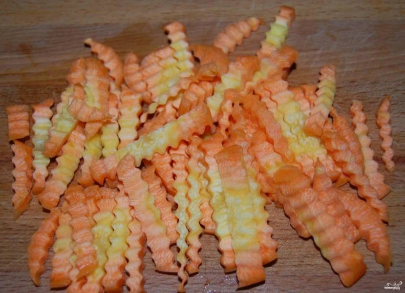 Помойте и очистите морковь. Порежьте морковку небольшими брусками. В сковородку положите жир из тушенки. На него выложите морковь, обжарьте 5 минут.