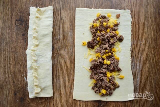 Тесто раскатайте и разрежьте на две части. В центр каждой насыпьте тертого сыра, разложите начинку из фарша. Защипните края теста вдоль по центру.