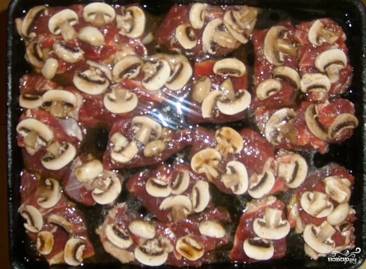 На кусочки мяса выкладываем нарезанные грибы. 