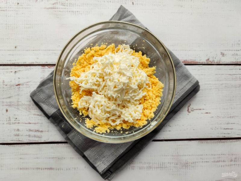 Плавленый сыр натрите на мелкой терке и добавьте к желткам.
