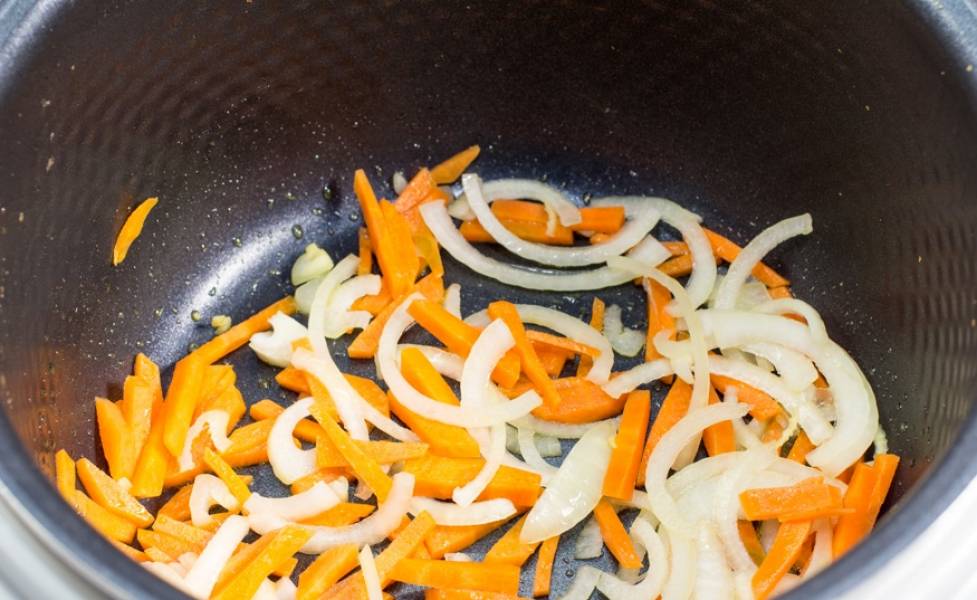 В чашу мультиварки наливаем небольшое количество растительного масла и включаем режим "Жарка". Выкладываем в мультиварку нарезанный полукольцами лук и морковь, нарезанную брусками. Обжариваем овощи несколько минут до полуготовности.