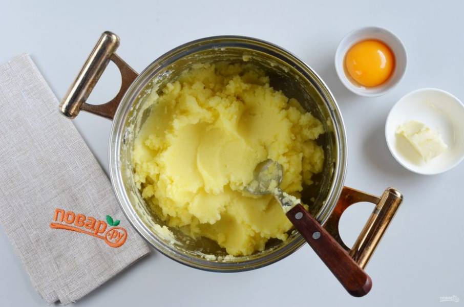 С готового картофеля слейте всю жидкость, она не понадобится. Добавьте белок яйца (желток я отложила для смазывания пирога) и сливочное масло (15 грамм). Толкушкой превратите в пюре и отрегулируйте на соль, по желанию добавьте перец черный молотый.