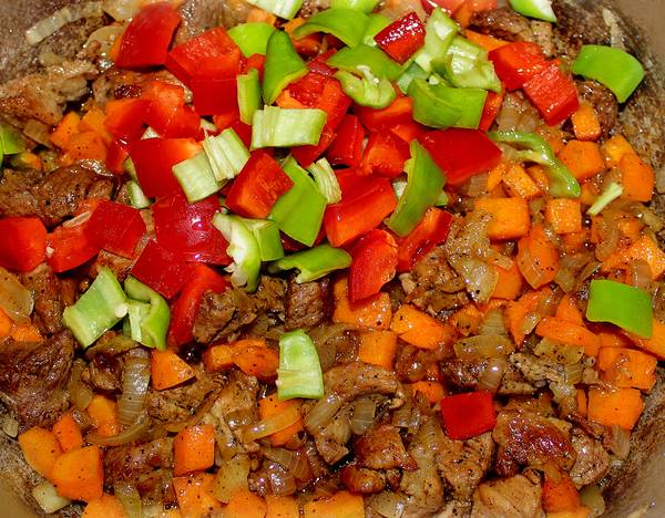 Очищаем перец от сердцевины, морковь чистим. Нарезаем овощи небольшими кубиками и добавляем к мясу. Перемешиваем и обжариваем минут 5.