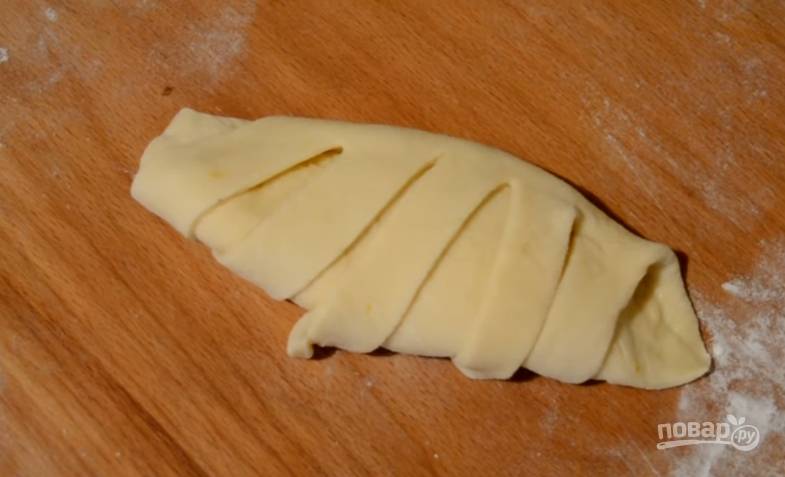 9. Каждую раскатайте в тонкую лепешку, ложку крема выложите почти по центру, накройте одной частью теста, а вторую ножом нарежьте полосками по 1 сантиметру, заверните полоски на тесто. 