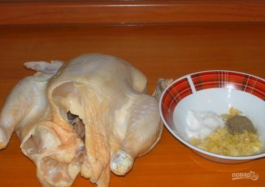 1.	Курицу (у меня около 1,7 килограмм) мою и вытираю салфетками. Чищу чеснок и выдавливаю зубчики в миску, добавляю соль и черный перец.