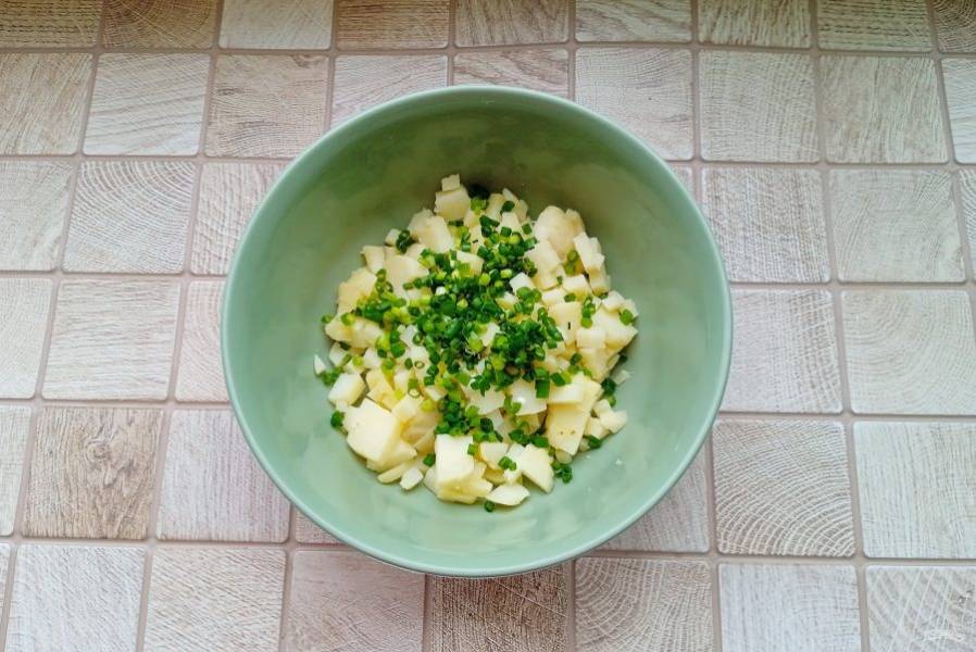 Картофель отварите, охладите, очистите и нарежьте небольшими кубиками. Зеленый лук помойте и мелко нарежьте. Выложите эти ингредиенты в миску.