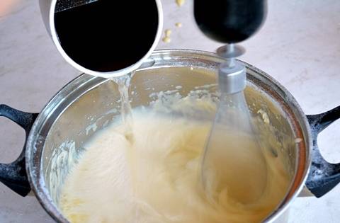 Опустите в тесто венчик для взбивания и включите миксер на полную мощность. Вскипятите чистую питьевую воду. Добавляйте тонкой струйкой кипяток в тесто, не переставая его взбивать. 