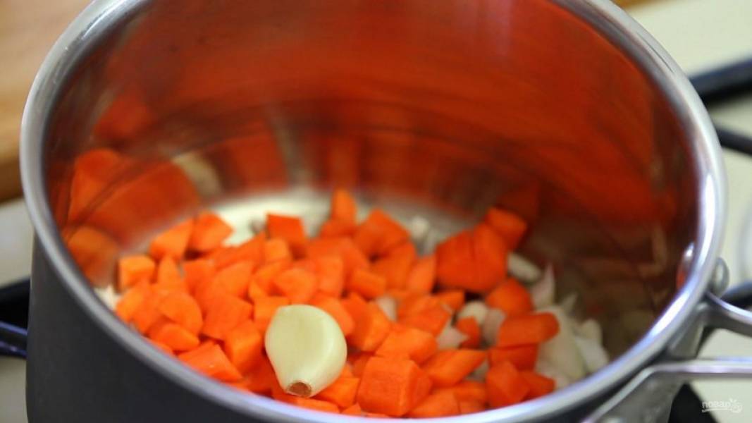 2. Затем овощи выложите в масло в кастрюле. Добавьте целый зубчик чеснока. Обжарьте ингредиенты в течение 5 минут до мягкости.