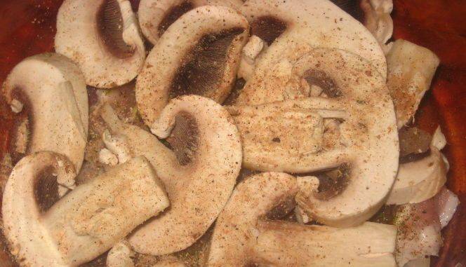3. Теперь солим и перчим мясо, после чего выкладываем нарезанные грибы, снова промазываем майонезом, а следующим слоем станет лук (кольцами).