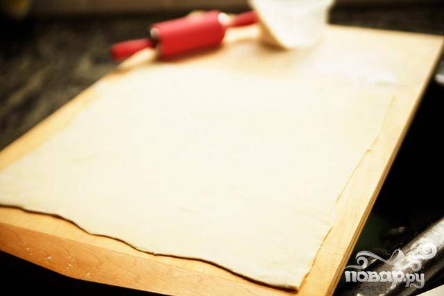 1. Разогреть духовку до 200 градусов. Выстелить противень силиконовым ковриком или пергаментной бумагой. На слегка посыпанной мукой поверхности раскатать лист слоеного теста, чтобы он стал достаточно тонким. Старайтесь сохранять квадратную форму, насколько это возможно. Периодически проверяйте, не прилипает ли тесто к поверхности, и добавьте дополнительно муку в случае необходимости.