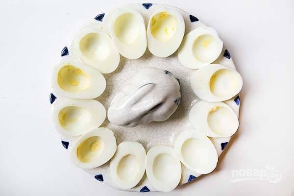1.	Положите яйца в кастрюлю с холодной водой, вода должна покрывать яйца на 2-3 см. Поставьте кастрюлю на огонь и доведите до кипения, затем выключите огонь, накройте крышкой и отставьте на 10-12 минут. Далее слейте кипяток и залейте холодной водой, чтобы яйца хорошо чистились. Почистите яйца, разрежьте их пополам по длине и удалите желток. Выложите половинки яиц на блюдо.