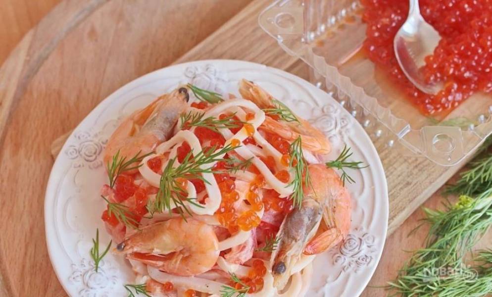 Выложите на блюдо маринованные креветки, отварные кальмары и нарезанную рыбу. Добавьте к салату красную икру, полейте заправкой. Украсьте веточками укропа и целыми креветками. 