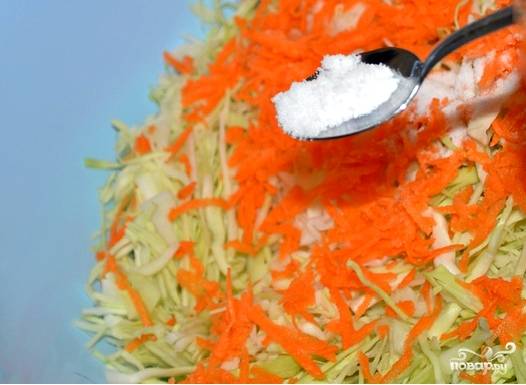 В тазике перемешиваю нашинкованную капусту с натертой морковью. Беру соль. Посыпаю все четырьмя столовыми ложками именно каменной соли. Такая соль лучше консервирует продукты.