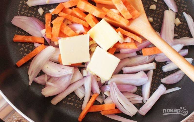 В отдельной сковороде растопите еще один кусочек масла. Лук очистите и нарежьте продольно, чтобы получились тонкие перышки. Обжарьте его вместе с нашинкованной соломкой морковью и чесночком. 