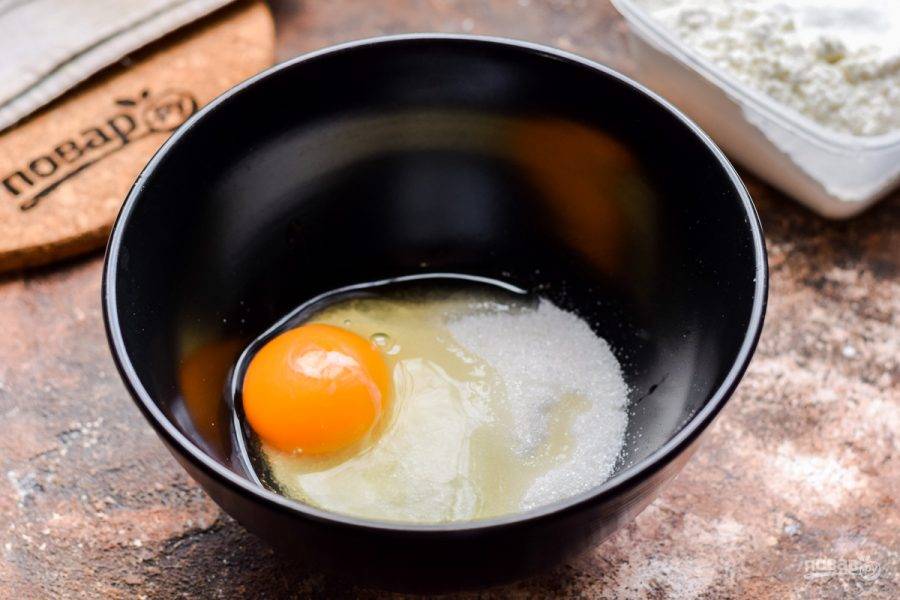 Сахар переложите в глубокую миску, добавьте куриное яйцо и небольшую щепотку соли.