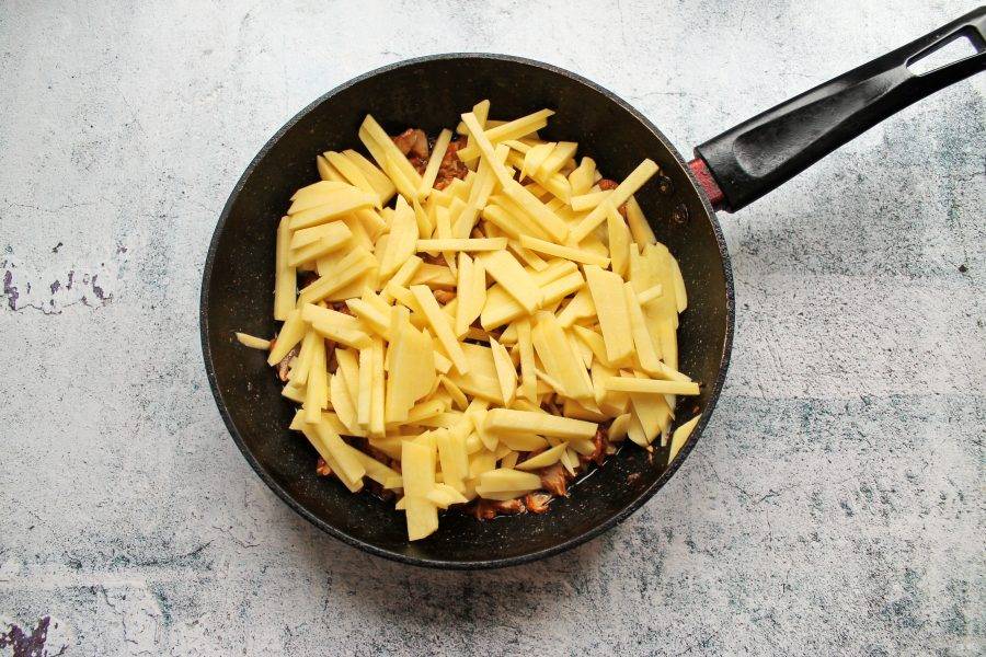 Очищенный картофель порежьте соломкой, сполосните и дайте воде полностью стечь. Выложите картофель в сковороду с грибами и луком.