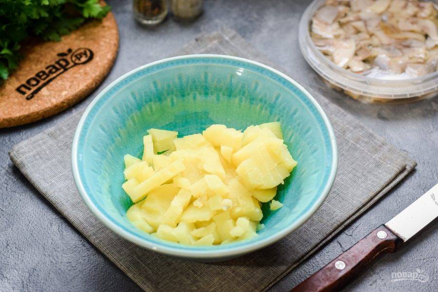 Картофель отварите заранее в мундире, после остудите и почистите. Нарежьте картофель небольшими кубиками и переложите в салатник.