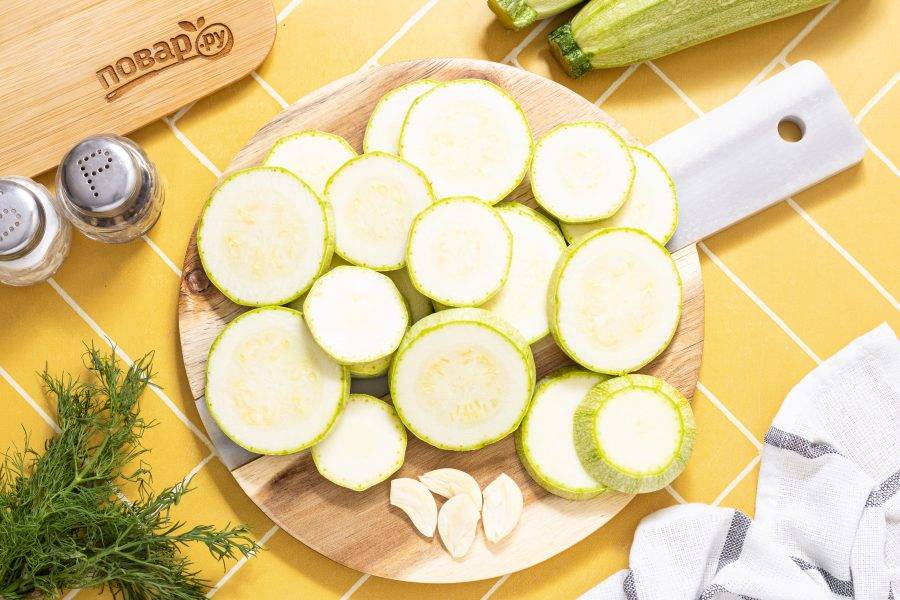 Кабачки нарежьте кружочками толщиной примерно 0.5 см. Если кабачки крупные, то кружочки можно разрезать пополам. Чеснок очистите от шелухи, разрежьте пополам.