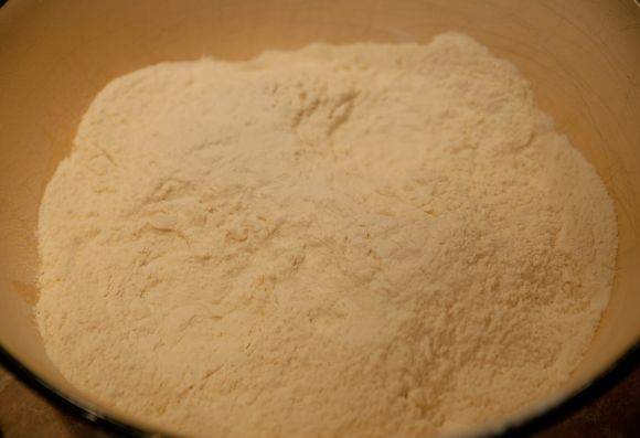 В отдельную миску просеиваем муку. Добавляем щепотку соли. Постепенно тонкой струйкой добавляем смешанную с дрожжами и сахаром воду. Вымешиваем тесто, пока оно не станет блестящим и эластичным.