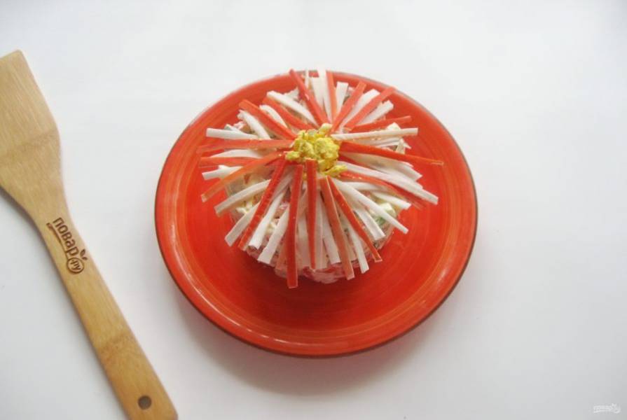 Выложите салат на тарелку. Нарежьте крабовые палочки тонкой соломкой и украсьте в виде хризантемы. Серединку цветка сделайте из яичного желтка.