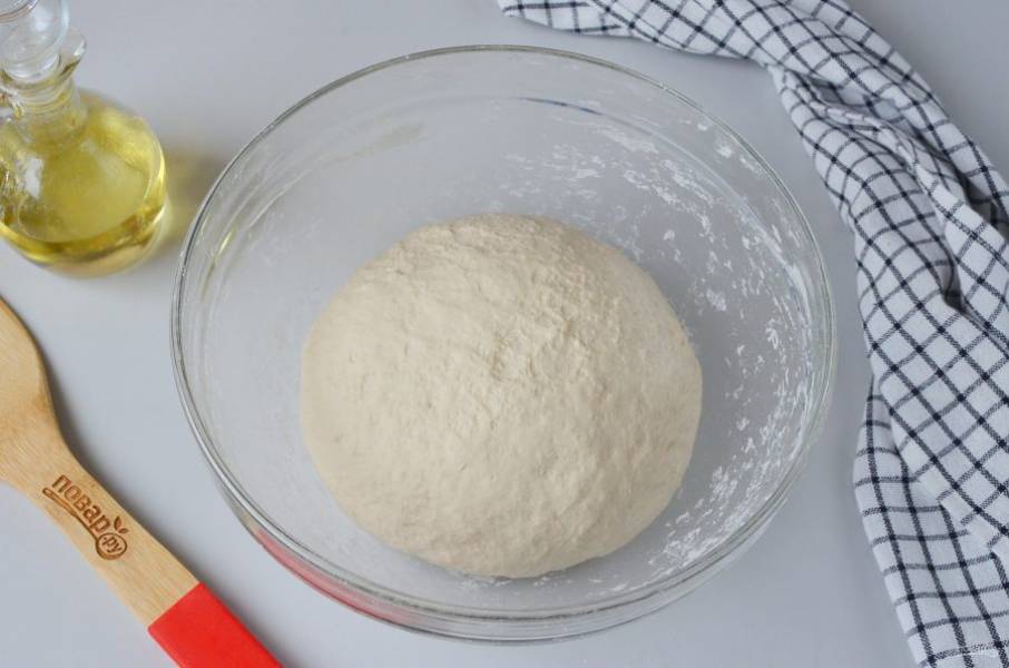 Когда тесто начнет собираться в ком, добавьте ложку растительного масла, вымешайте на столе еще 5-7 минут, пока не образуется упругий и пластичный колобок. Верните тесто в миску.