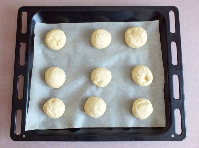 Разделите тесто на 9-12 частей. Подкатайте в шарики. Противень застелите пекарской бумагой. Выложите заготовки на противень. Прикройте полотенцем и оставьте на 15 минут для подъема.