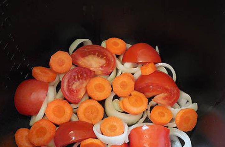 Крупно порежьте овощи и мясо. Налейте на дно чаши мультиварки немного растительного масла и выложите овощи и мясо слоями. Сначала выложите лук, морковь и половину помидор. 