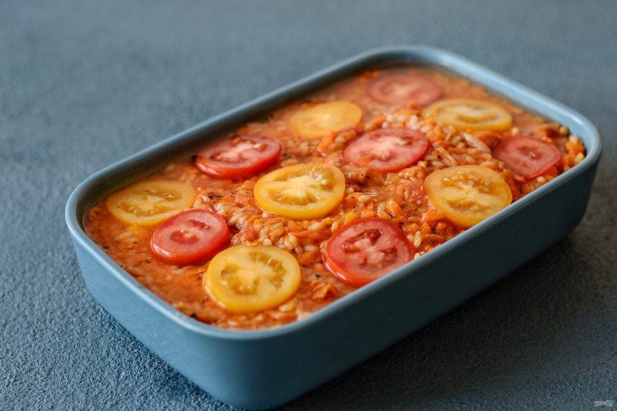Сверху выложите рис с овощами. Украсьте кружочками томатов. Налейте ещё немного воды и поставьте выпекаться в духовку на 20 минут при температуре 180 градусов. 