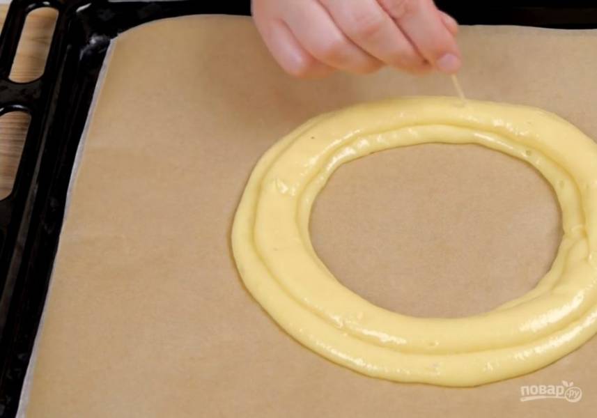4. Переложите тесто в кондитерский мешок и выдавите на бумагу для выпечки три кольца диаметром 13 см (один на другой). Пузырьки уберите зубочисткой. Сверху смажьте яйцом и посыпьте миндалем. Выпекайте в разогретой до 180 градусов духовке 40 минут. 