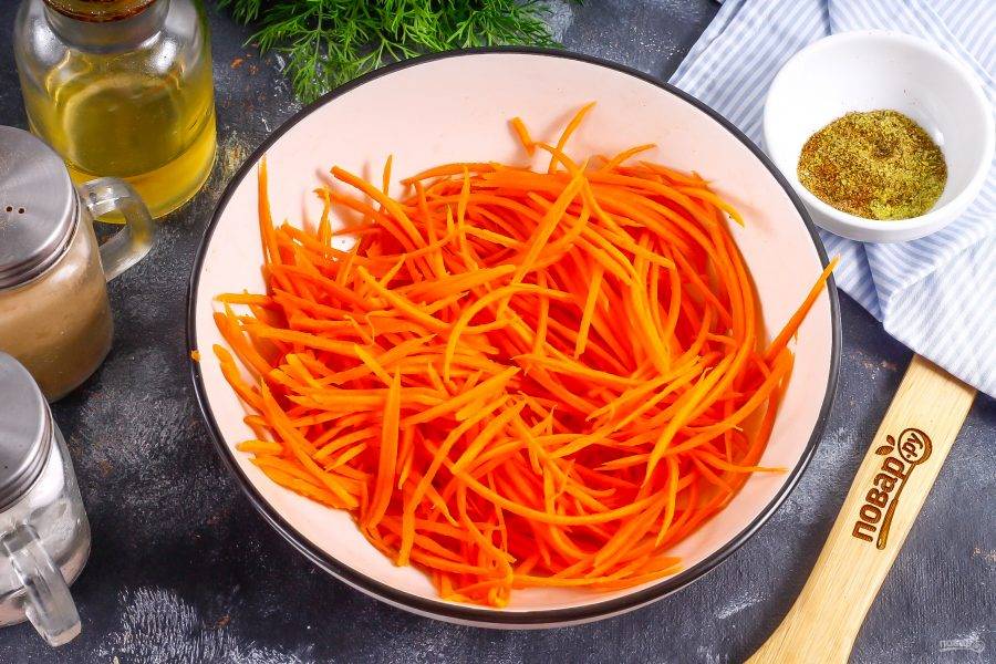 Морковь очистите от кожуры вместе с луком и чесноком, промойте. Натрите морковь в глубокую емкость на терке для моркови по-корейски.