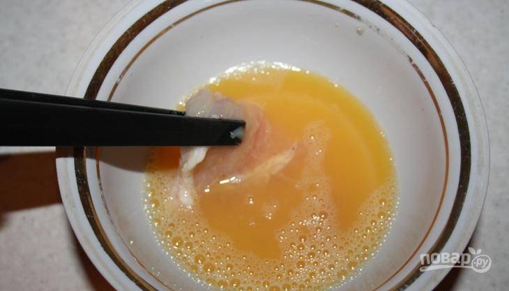 В пиалу вбейте сырое куриное яйцо, влейте к нему пятьдесят миллилитров воды и взбейте все вилкой или венчиком до однородности. Затем обмакните в яйцо кусочки курицы. 
