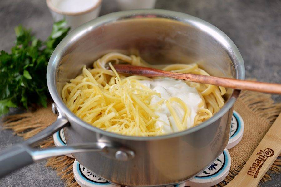 Верните спагетти назад в сотейник, добавьте сметану и тертый сыр, также влейте немного воды из чашки. Прогрейте соус на тихом огне, посолите и поперчите макароны по вкусу.