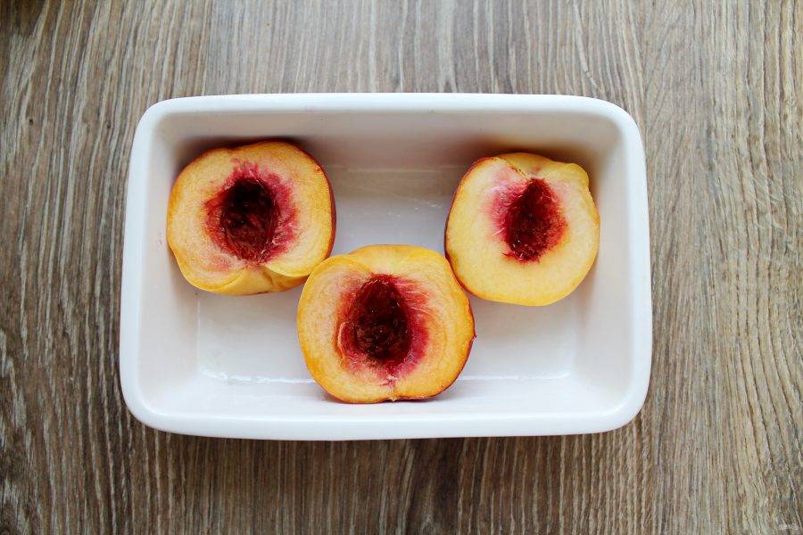 Персики разделите на две половинки. Форму смажьте немного маслом и выложите персики.