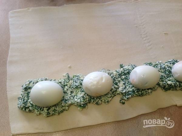 6. Отступив от края пласта примерно 5-6 см, выложим половину начинки и разложим отваренные яйца.