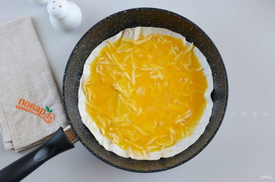 Сковороду нагрейте, смажьте растительным маслом, выложите лаваш, распределите половину сыра тертого, потом вылейте яйца.
