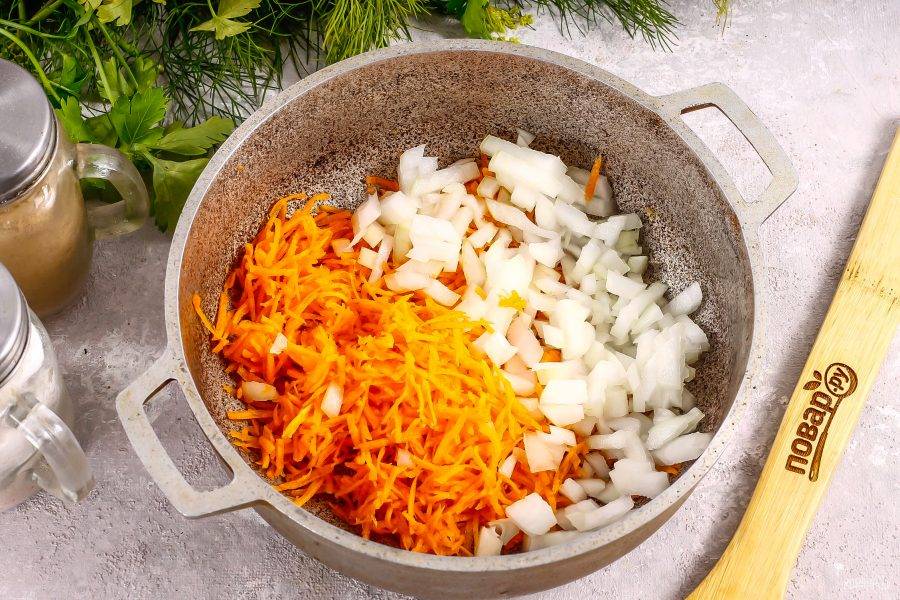Очистите и промойте морковь и лук в воде, нарежьте луковицу мелкими кубиками, а морковь натрите на терке с мелкими ячейками. Влейте в казан растительное масло, и обжарьте нарезки примерно 3-5 минут до румяности.